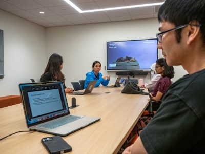 Xuan Wang talks to students around a conference table.
